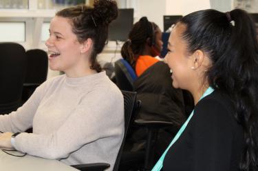 Two members of the customer services staff laugh whilst training in their office.