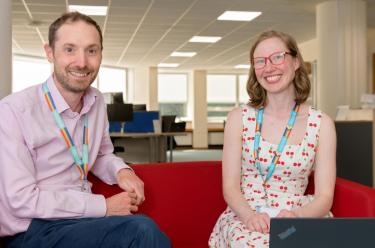 Coworkers sitting on a red sofa smiling